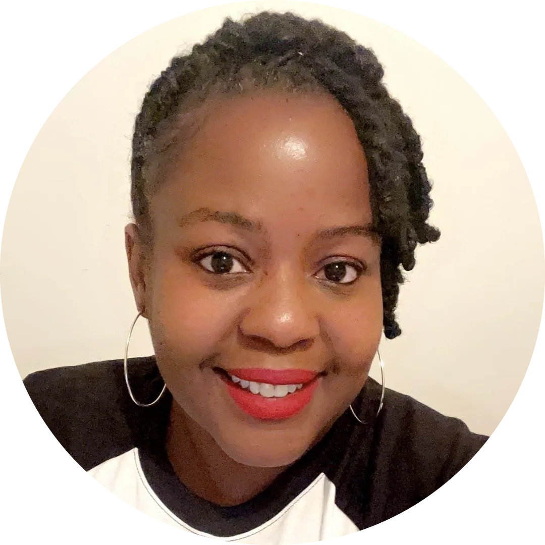 A smiling person with dark, curly hair styled in twists is wearing large hoop earrings and bright red lipstick. They are dressed in a black and white top and are positioned against a light-colored background.